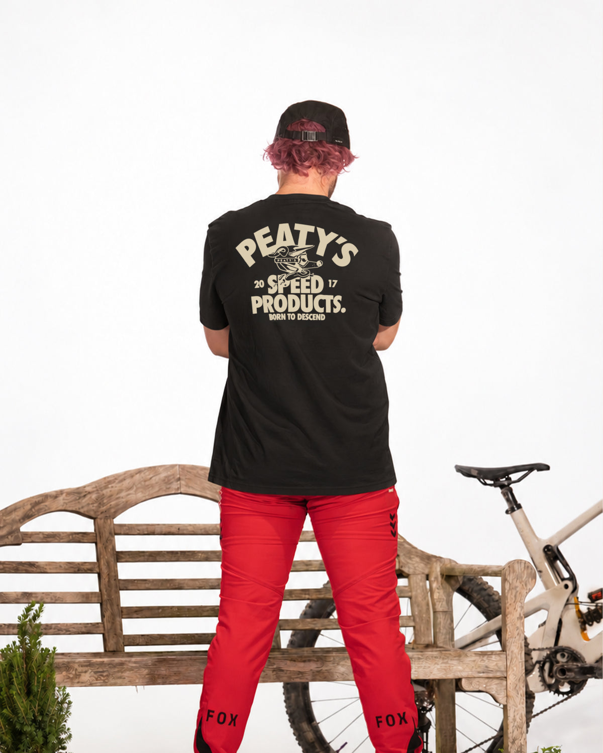 Rider wearing Black Peaty's Descend T-shirt with large back print beside a mountain bike