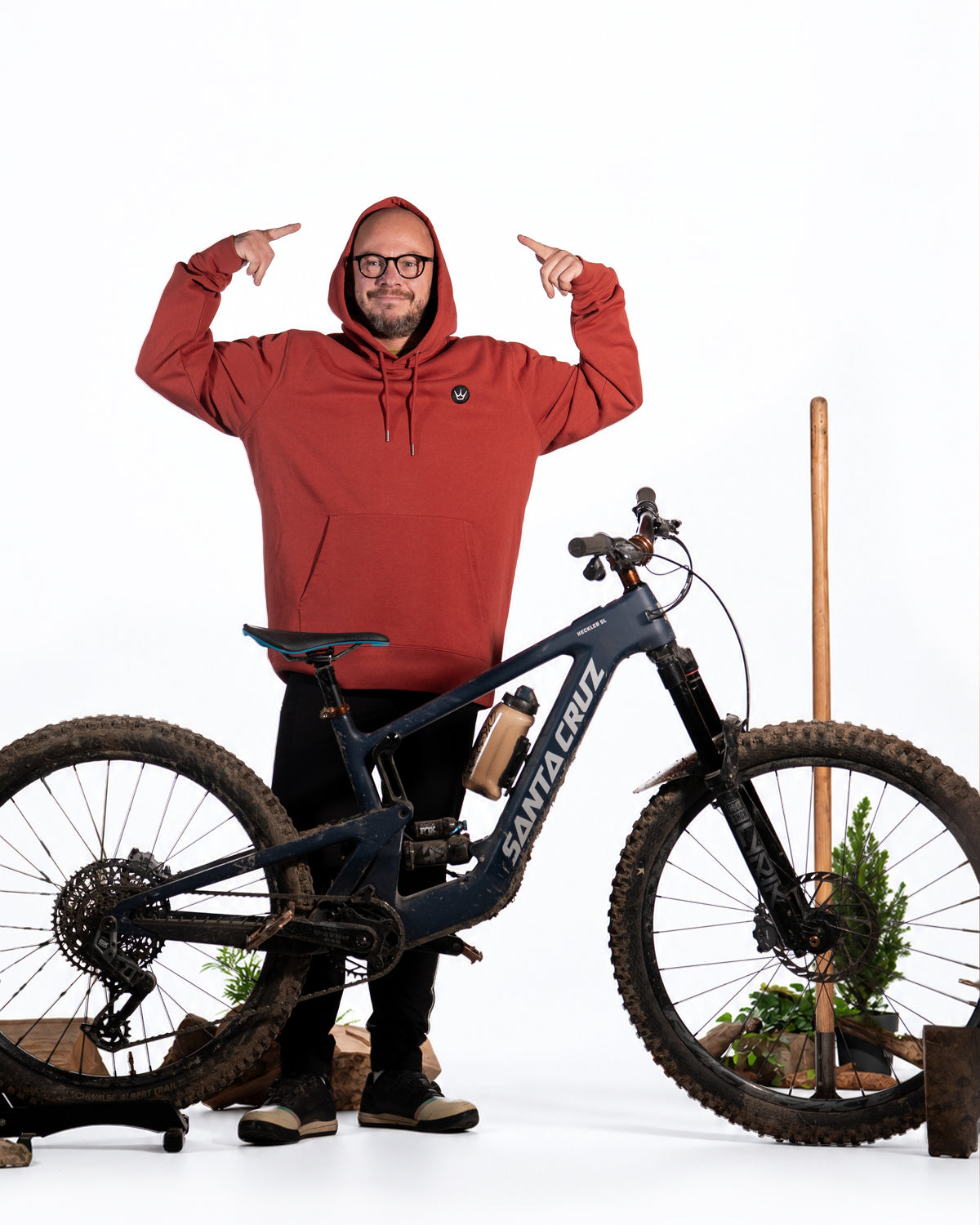 Rider wearing Earthy Red Peaty's Embroidered Crown Hoodie beside a mountain bike